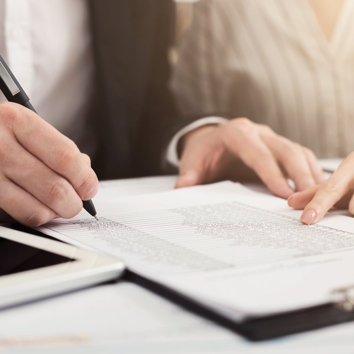 person writing with a pen on a clipboard in an office setting
