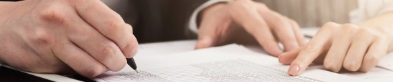 person writing with a pen on a clipboard in an office setting