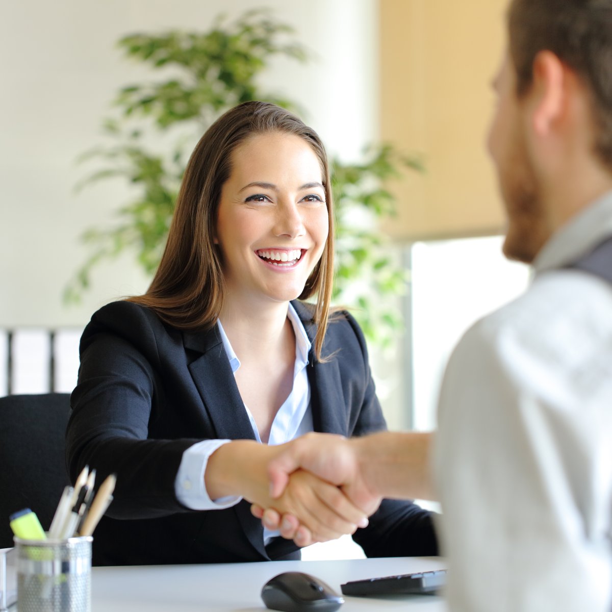 A woman shaking a man's hand while they are sitting across from eachother at a desk